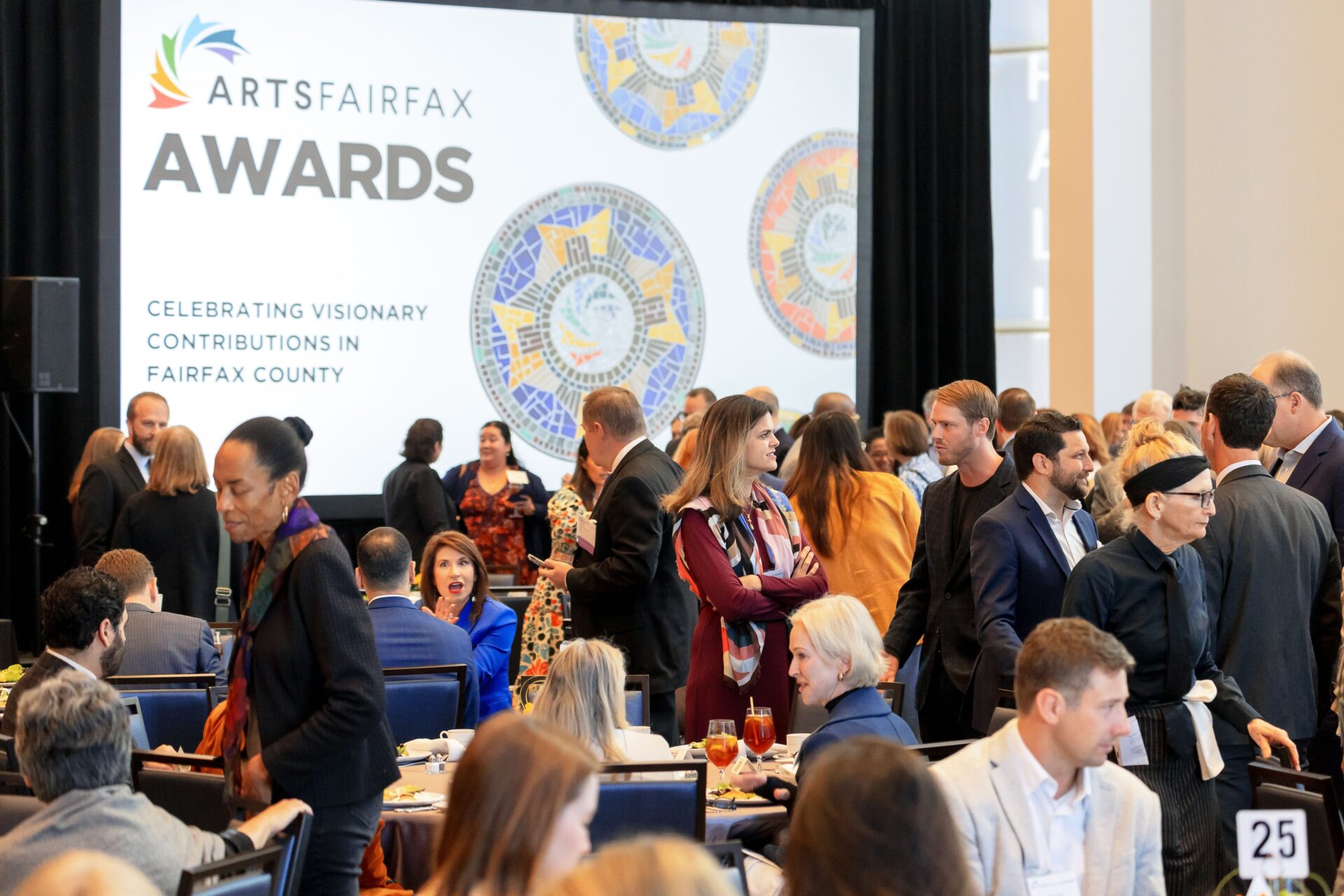 On a screen the words "ArtsFairfax Awards" appear alongside works of mosaic arts. In front of the screen