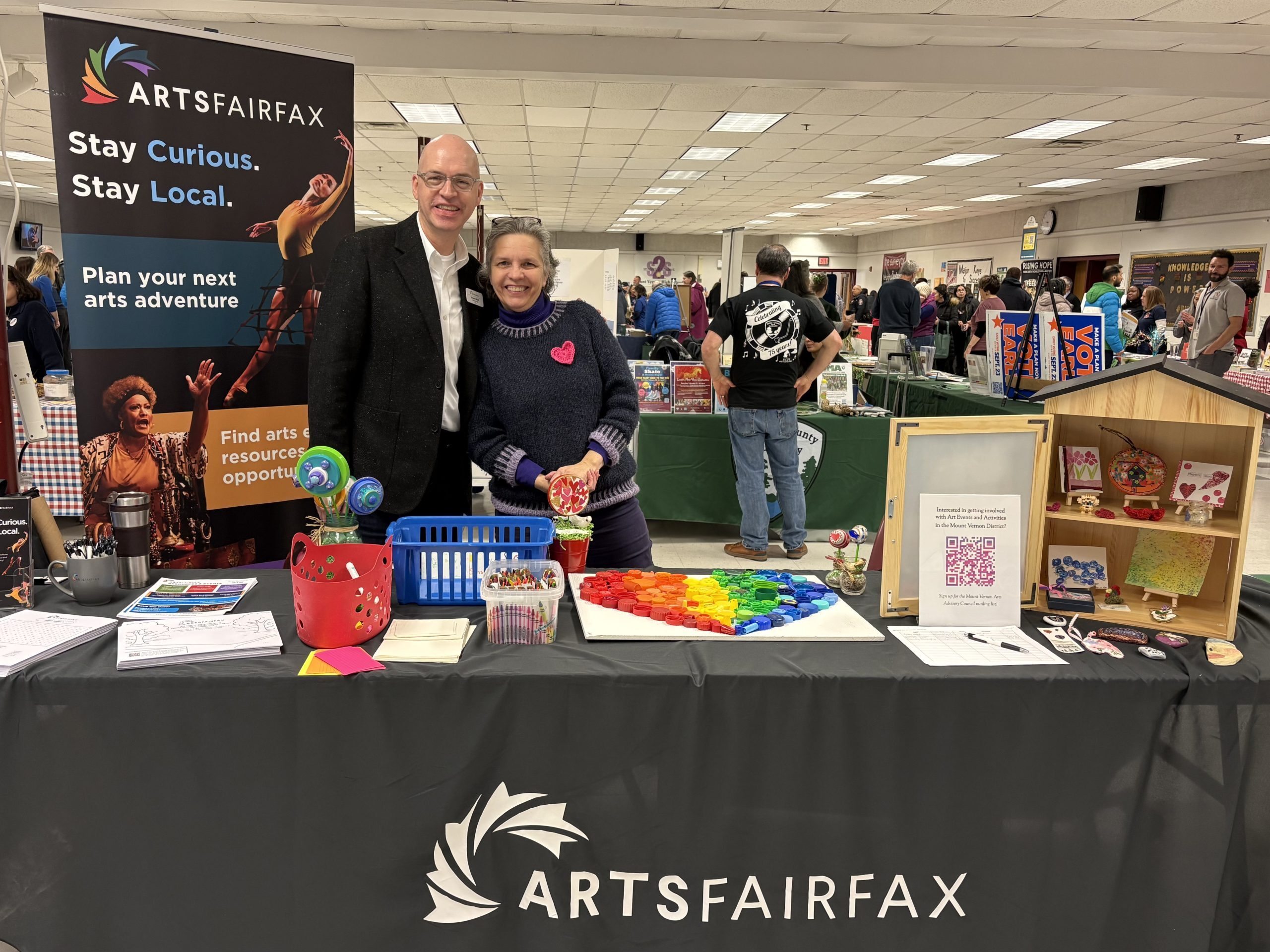 ArtsFairfax President & CEO Stuart Holt stands with Mount Vernon District Arts Advisory Council Chair Cathy Hosek at a table with a Free Little Art Gallery and promotional materials at the Mount Vernon District Town Hall.