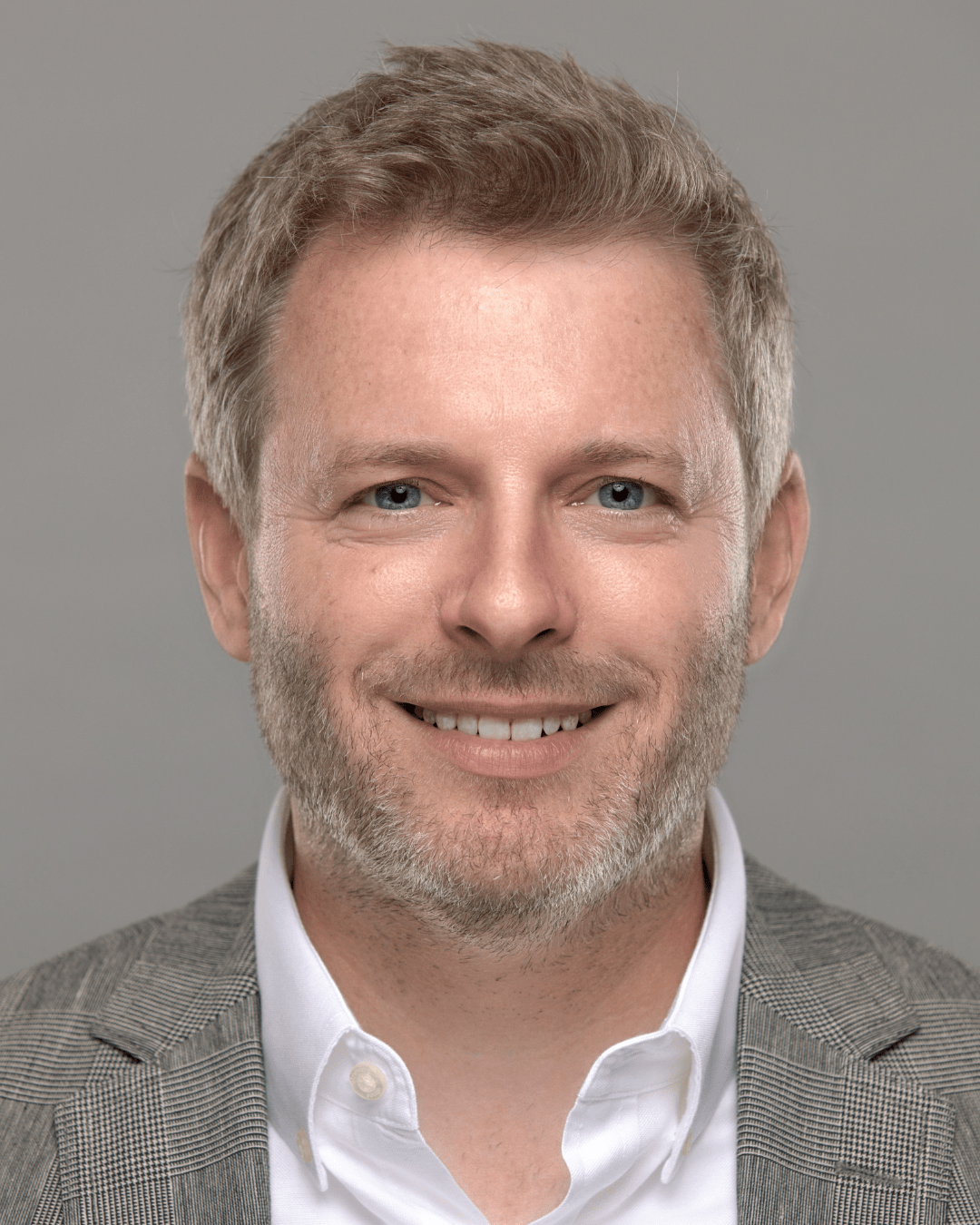 A man smiles in a headshot photo. He is wearing a white button shirt with a gray suit jacket.