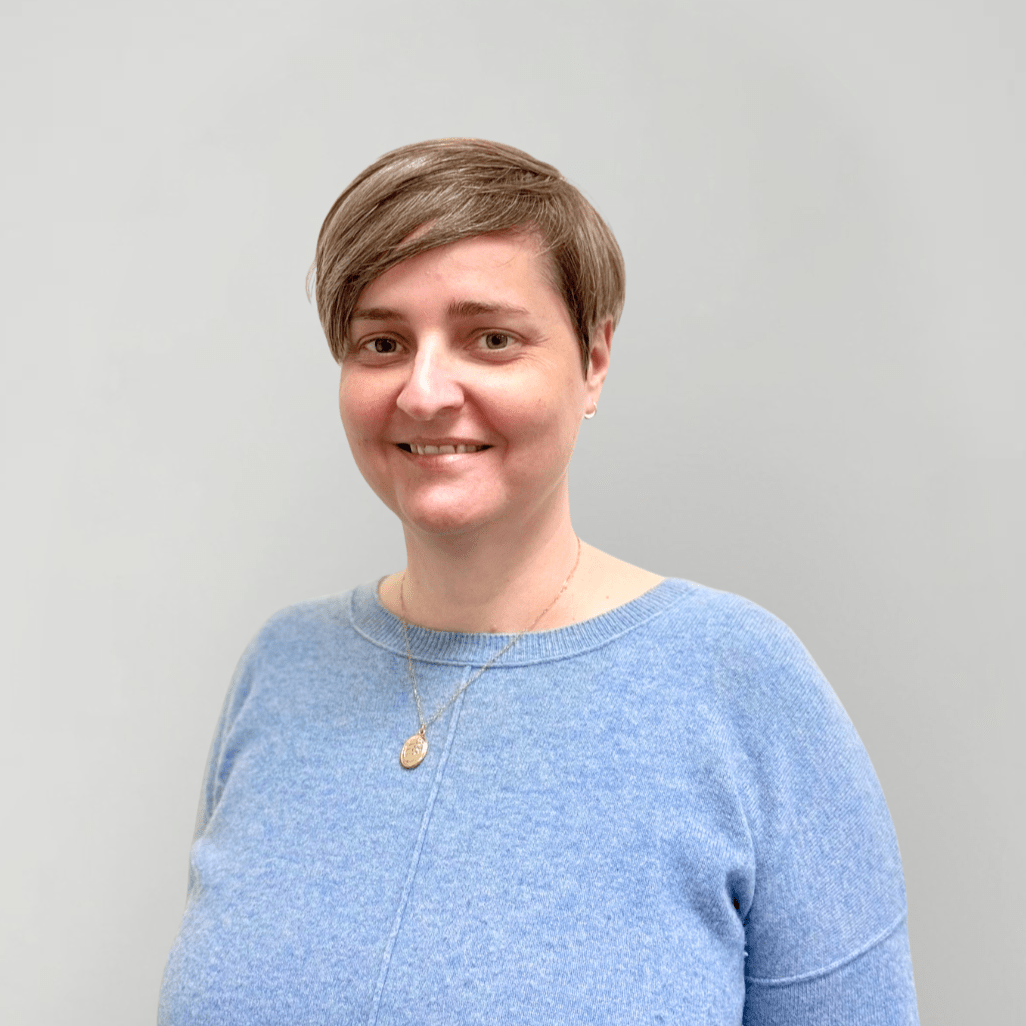 A woman with short hair and a light blue sweater smiling in a headshot photo