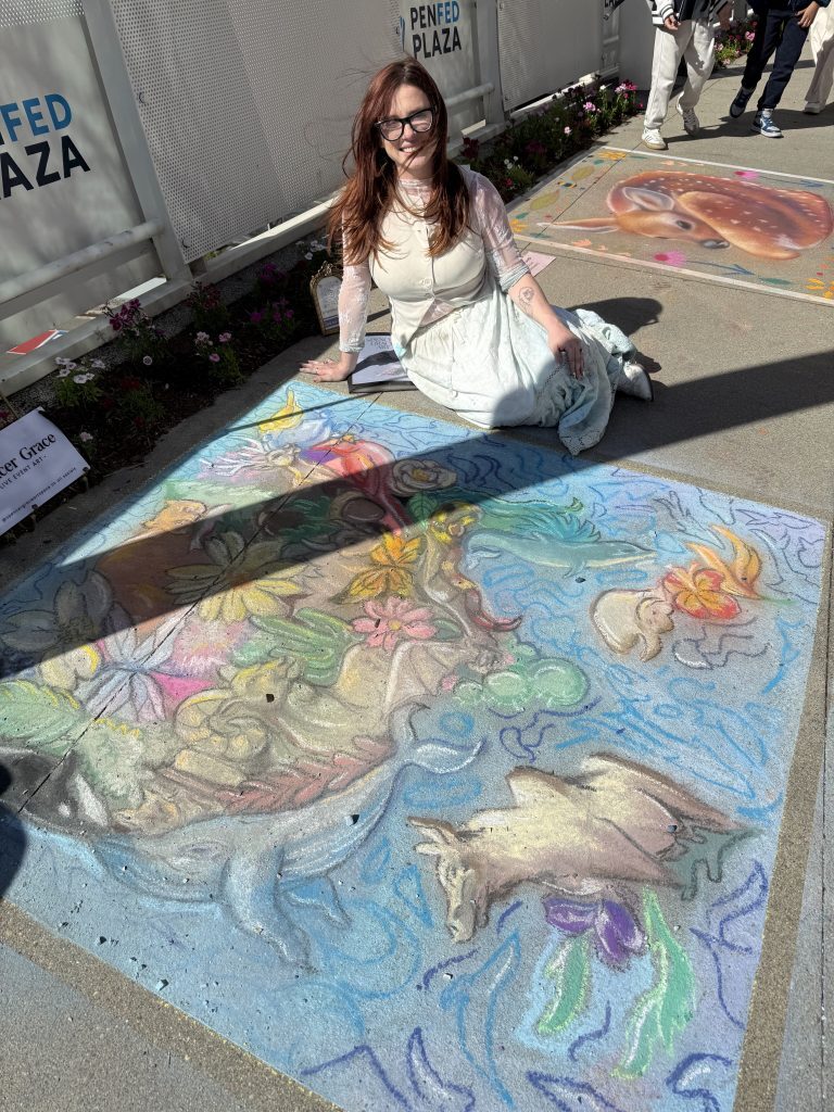 A woman with a white dress sits next to her chalk artwork featuring American flora and fauna on a paved plaza at Tysons Corner Center.