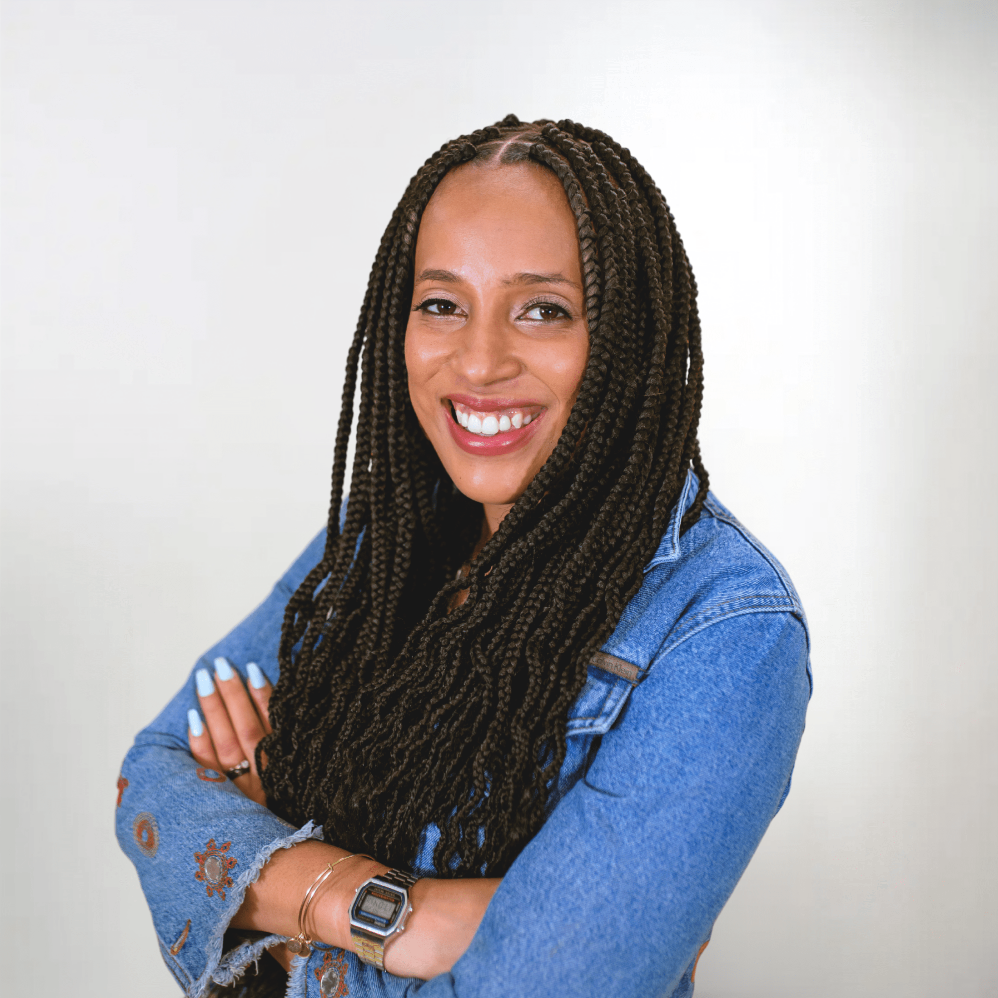 A woman with dark braided hair is wearing a jean shirt and smiles in a headshot photo.