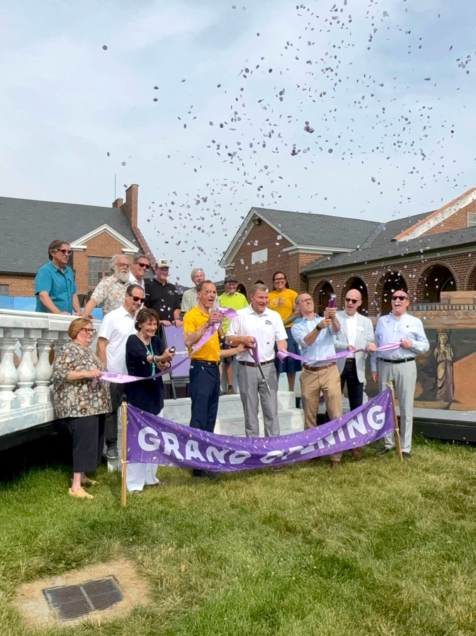 Artists and elected officials cut a purple ribbon that says "grand opening" at the Masterpiece Mini Golf grand opening at Workhouse Arts Center.